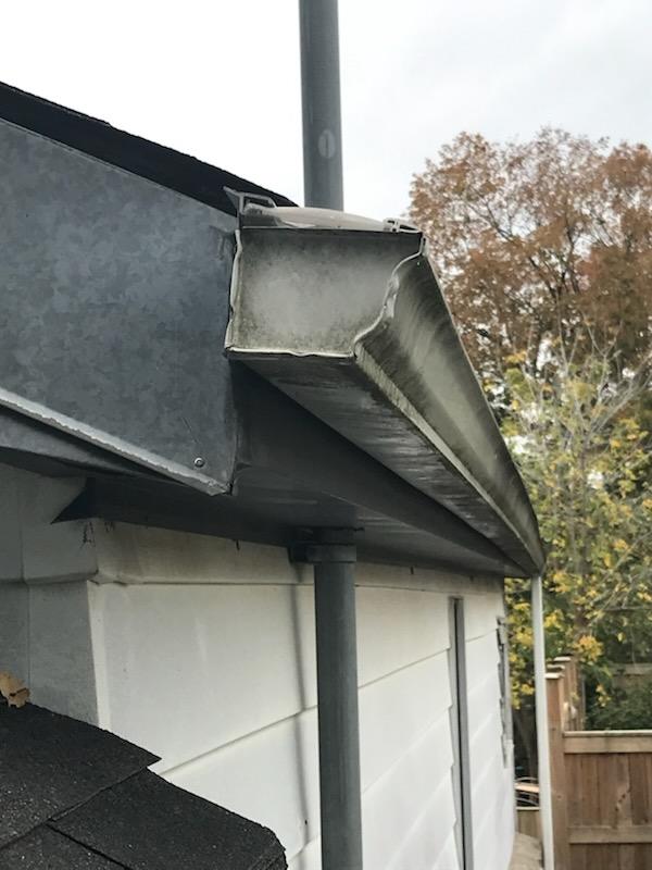 Reverse-curve metal gutter helmet on a low roof, due for replacement